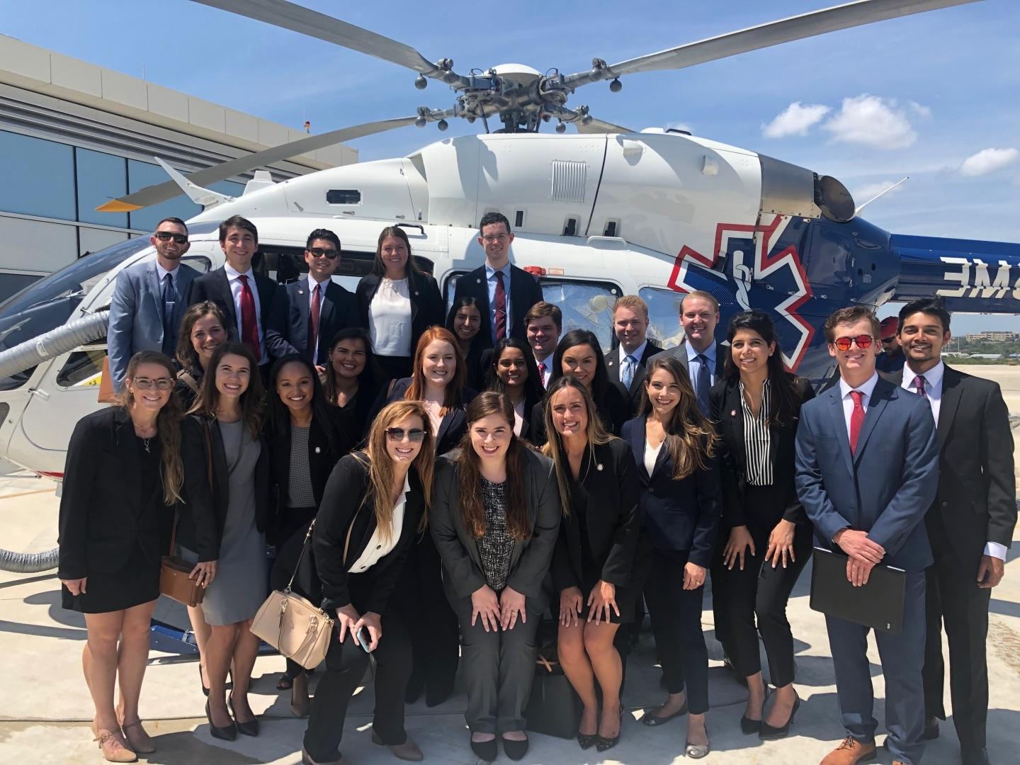 Graduate students gather in front of a rescue helicopter while visiting a local hospital.